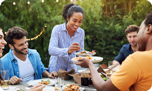 woman serves food to friends at a table during a summer dinner party